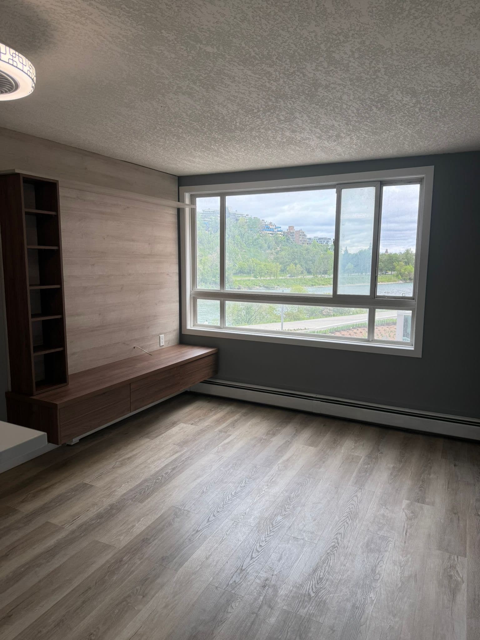 Living room with built-in light wood custom media console and shelving unit, featuring a large window with a scenic view by Calgary custom cabinets.