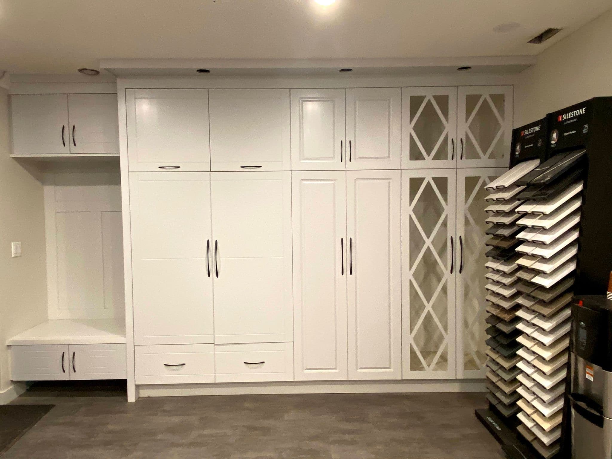 Modern white Calgary custom cabinets in an entry or mudroom design, featuring storage, a bench, and decorative mirrored doors, alongside Silestone countertop samples.