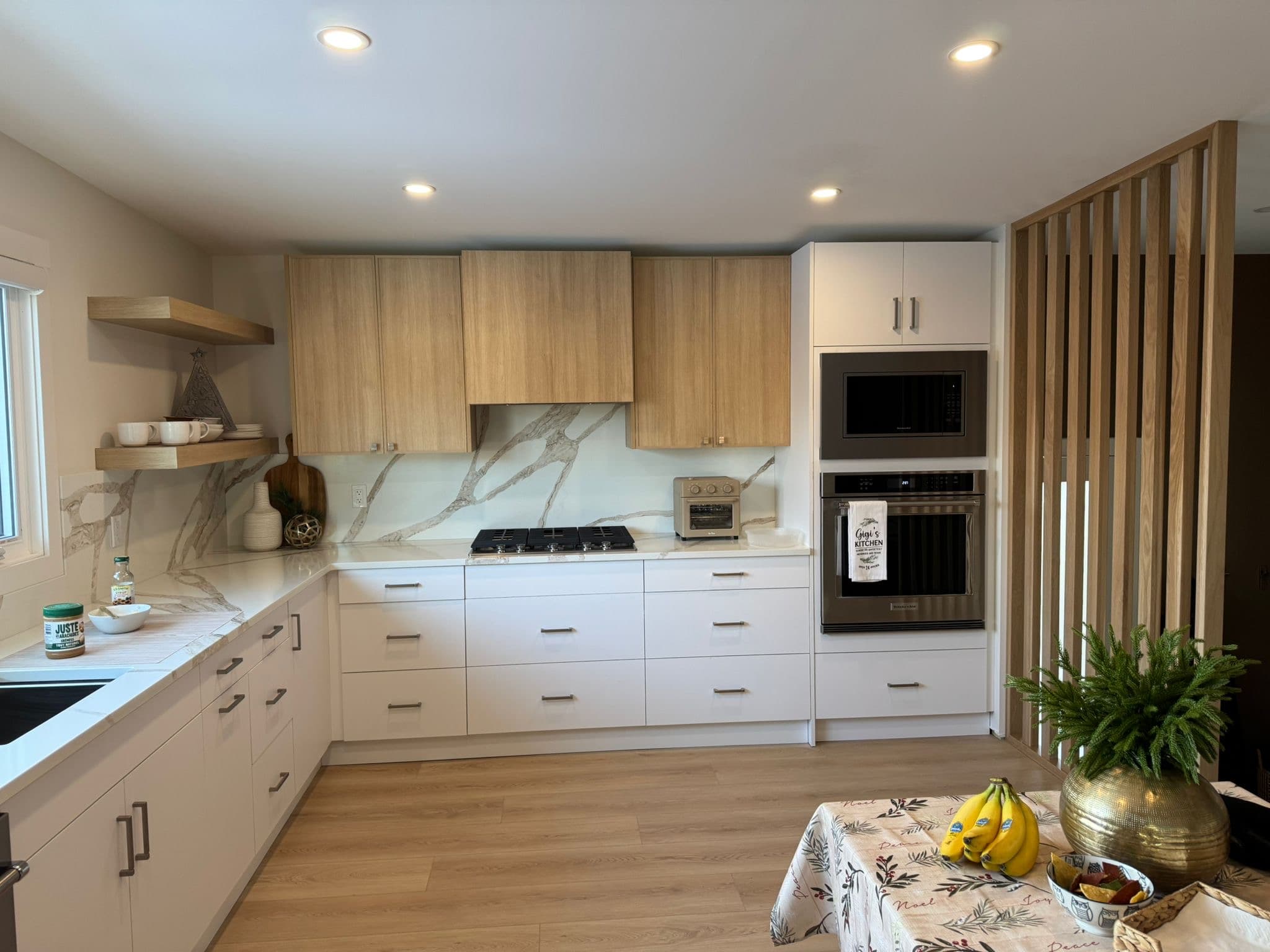 A modern kitchen design with two-tone Calgary custom cabinets, light wood upper cabinets and white base cabinets, quartz countertops, and a decorative wood room divider.