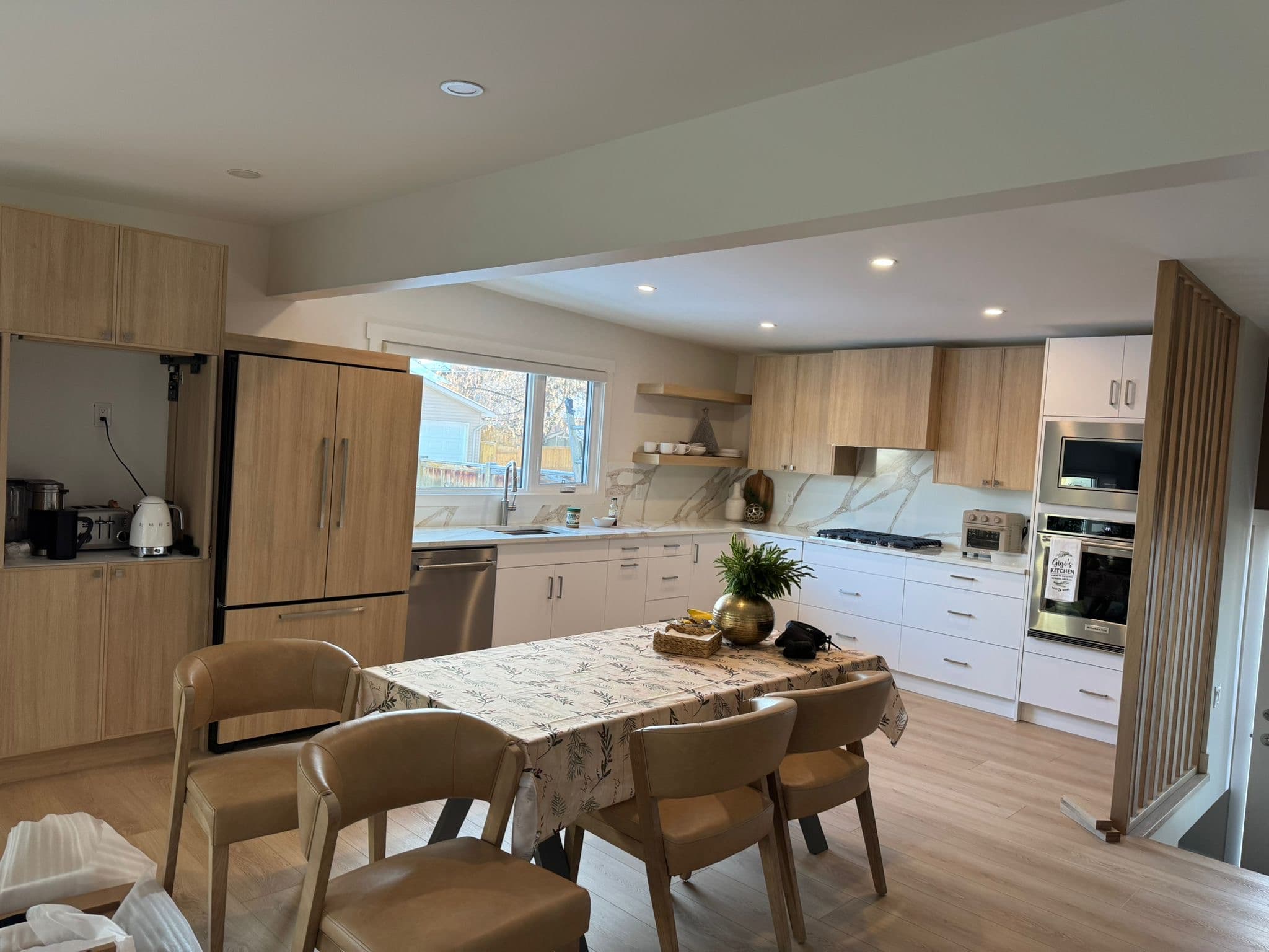 Stylish open-concept kitchen featuring two-tone light wood grain and white custom cabinets, an integrated refrigerator, and a dining area, by Calgary custom