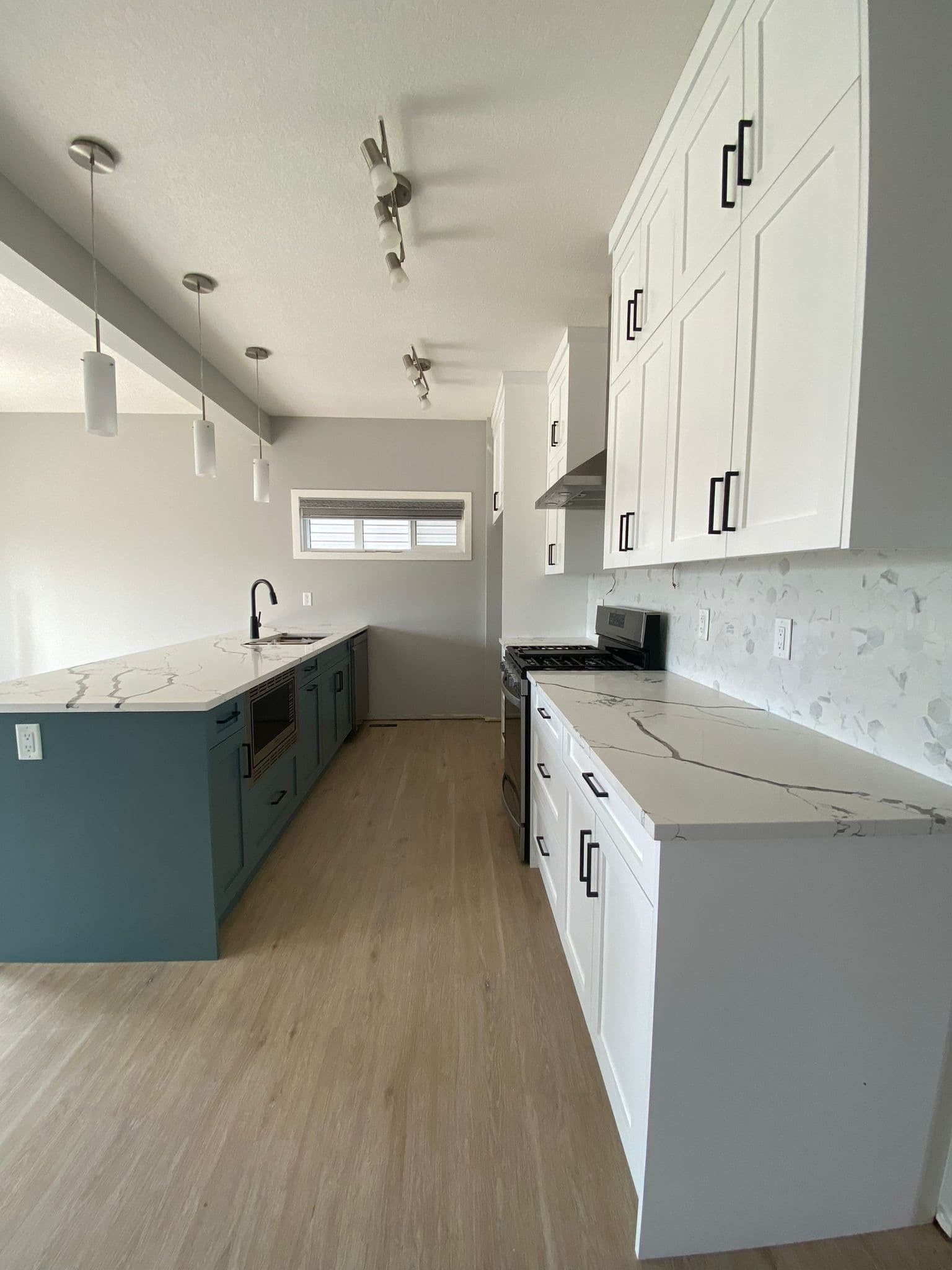 Modern kitchen with white upper cabinets, teal island, white quartz countertops, and light wood flooring. Calgary custom cabinets.
