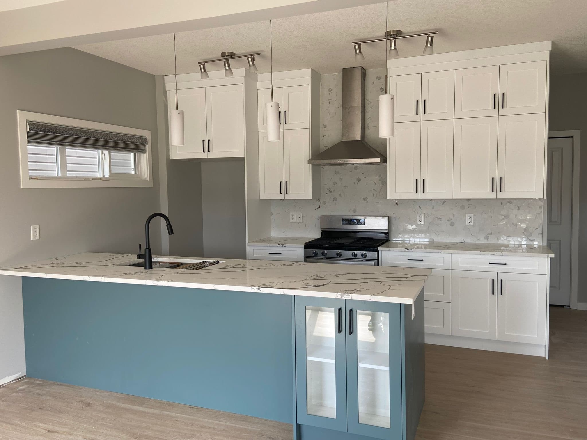 Modern kitchen featuring white upper and lower cabinets, a blue kitchen island with a quartz countertop, and pendant lighting, by Calgary custom cabinets.