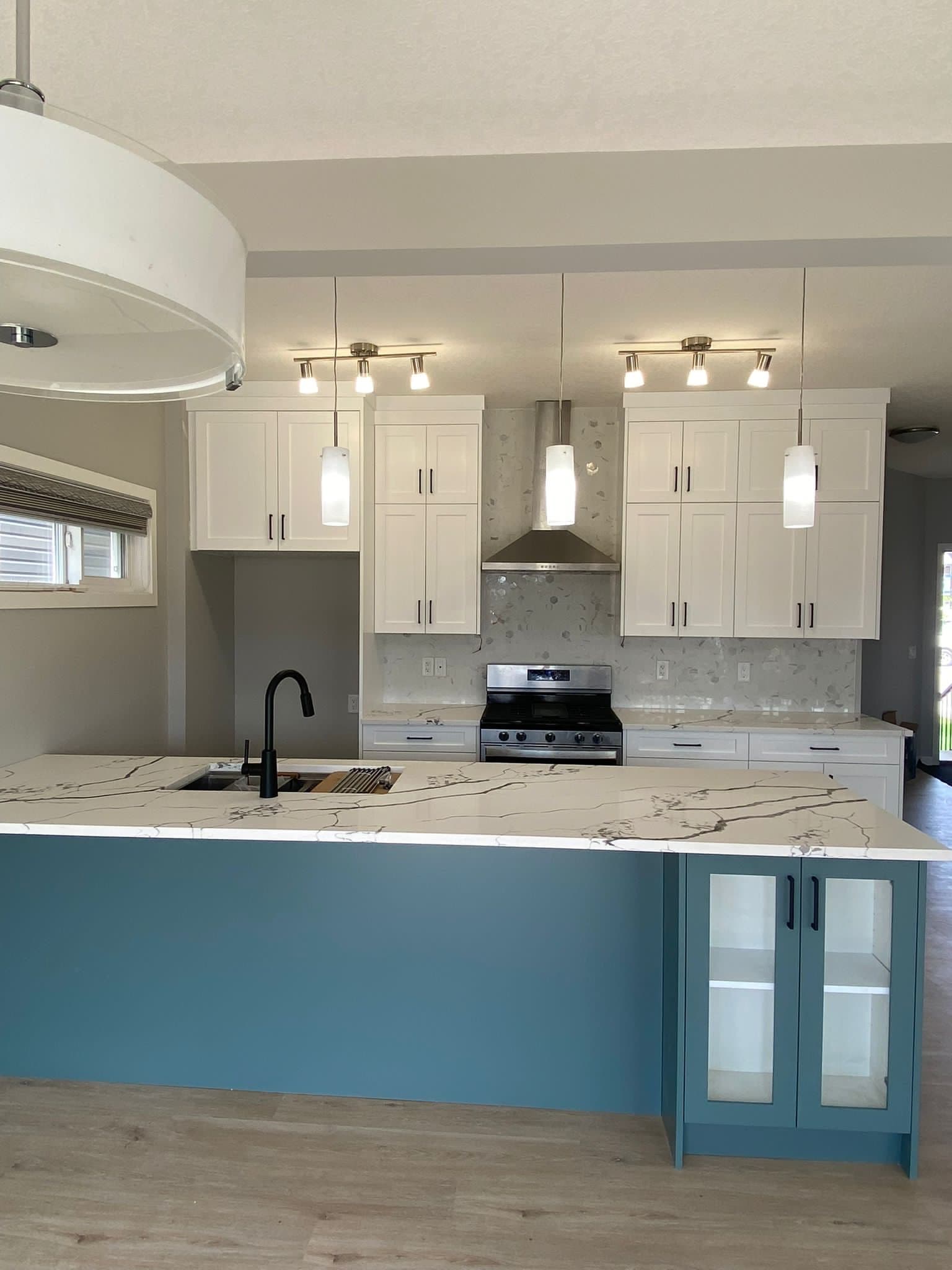 Modern kitchen featuring white shaker Calgary custom cabinets, a teal kitchen island with glass doors, white quartz countertops, and a black faucet.