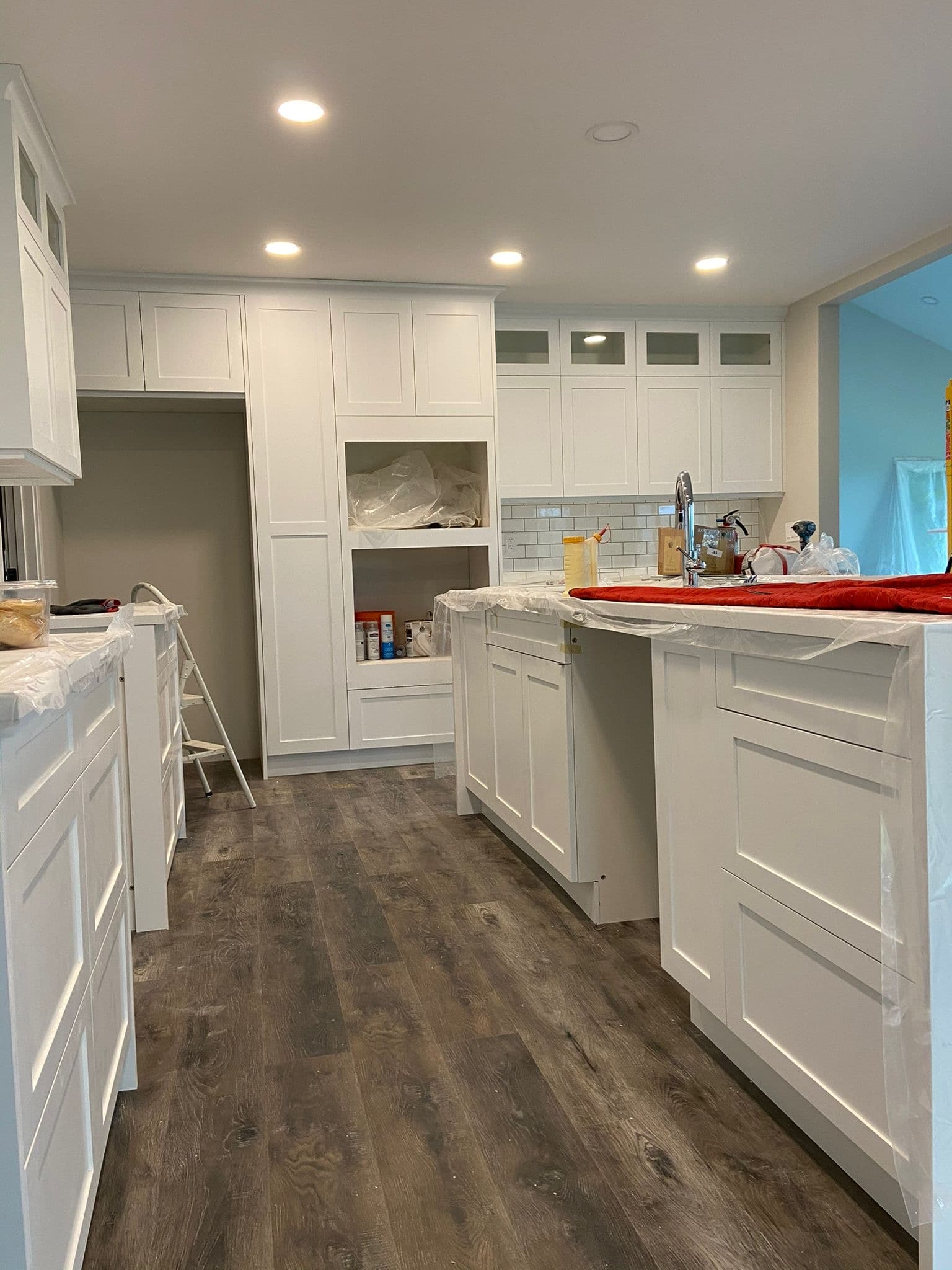 A newly renovated kitchen features crisp white shaker-style Calgary custom cabinets, a large central island, new dark wood flooring, and modern recessed lighting, giving a clean and bright aesthetic.