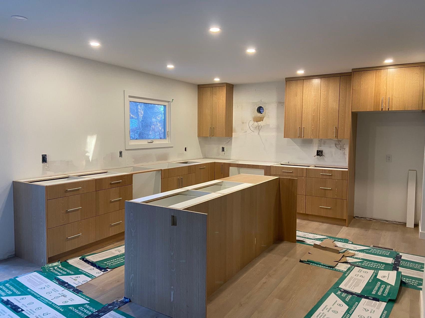 A bright kitchen under construction features light wood custom cabinets and an island, demonstrating the progress of Calgary custom cabinets installation.